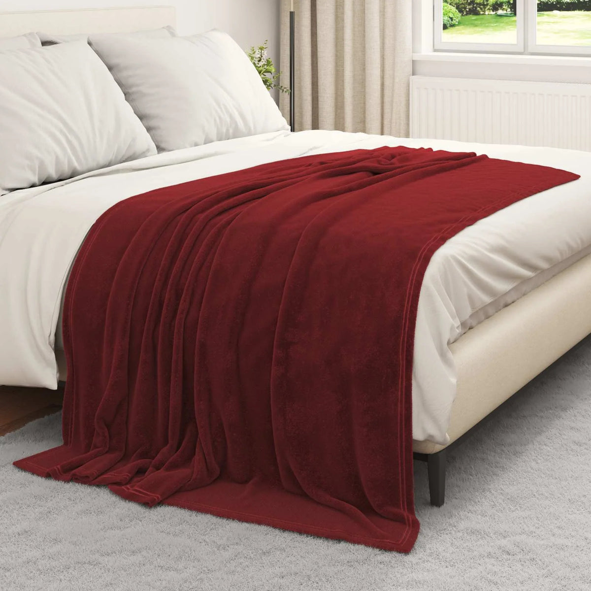 Couverture bordeaux présentée sur un lit blanc