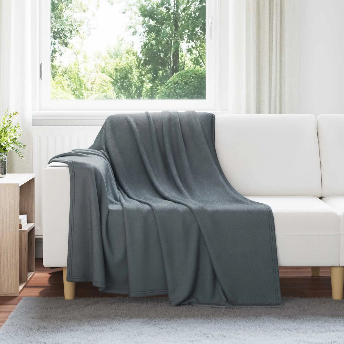 Couverture Chaude et Légère, coloris gris foncé, drapée sur un canapé blanc