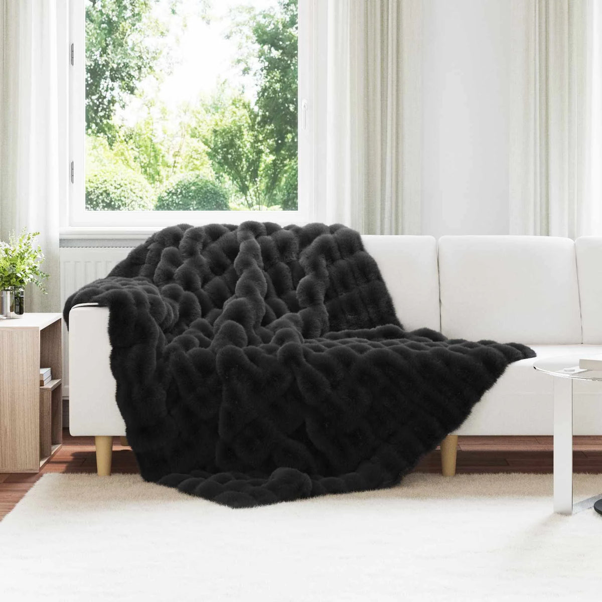 Couverture Fausse Fourrure Noire, coloris noir, drapée sur un canapé blanc