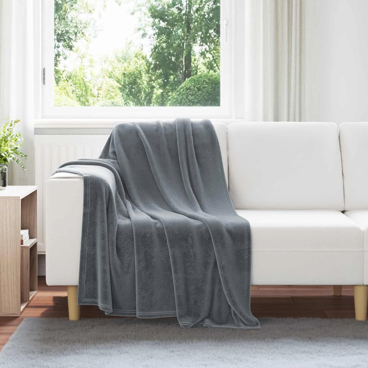 Couverture Polaire, coloris gris foncé, drapée sur un canapé blanc